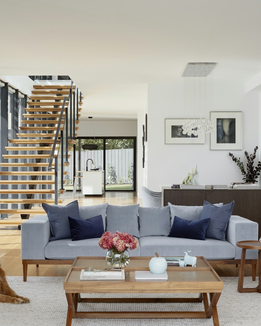 Warm, light-filled living room with a wood staircase and a golden retriever resting near the sofa